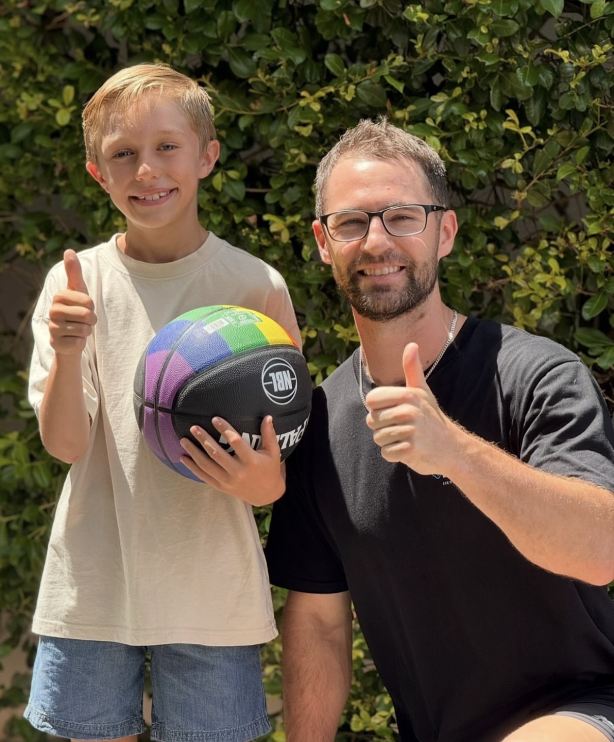 Isaac McCrimmon and a smiling child holding a basketball, both giving a thumbs up